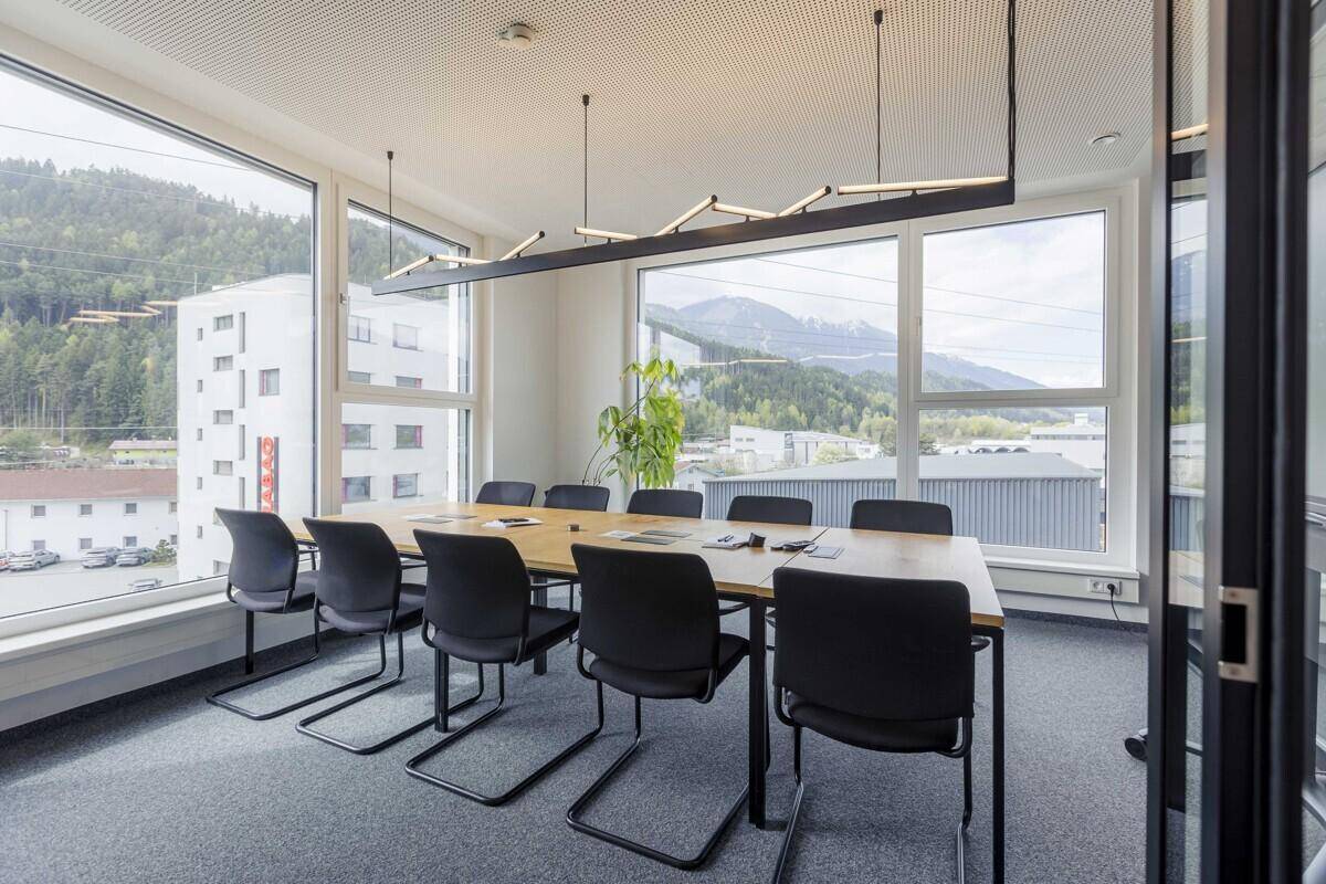 Heller Konferenzraum mit großem Holztisch, modernen Leuchten und Panoramablick auf die Berge.