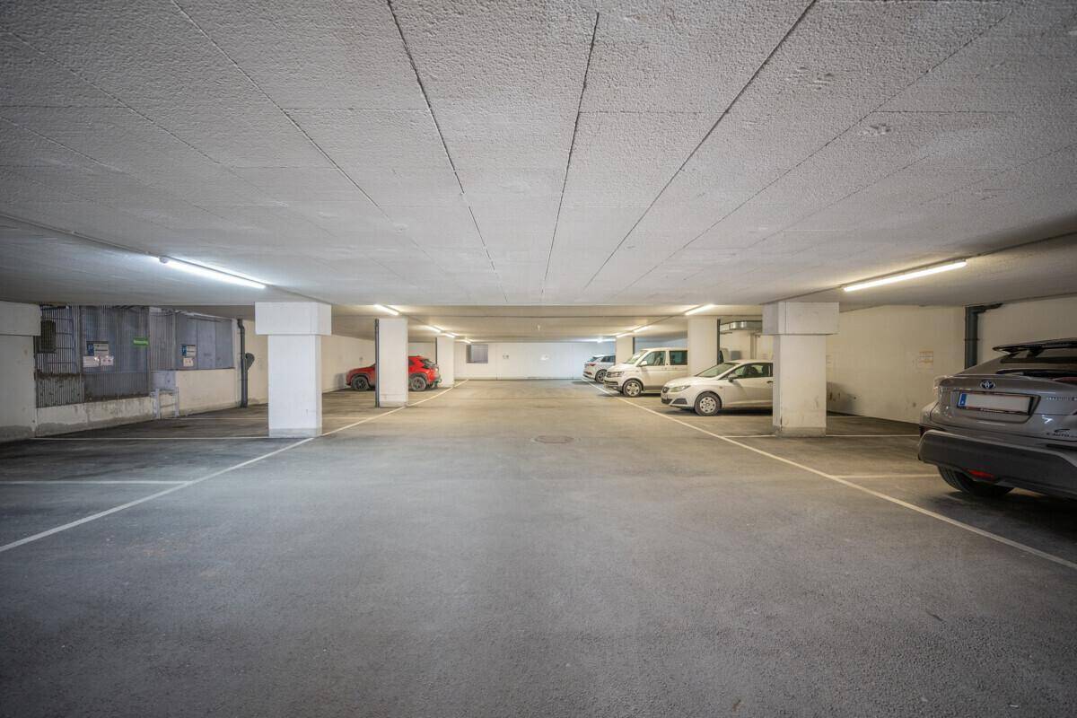 Geräumige Tiefgarage mit mehreren geparkten Autos, Betonboden und effizienter Deckenbeleuchtung.