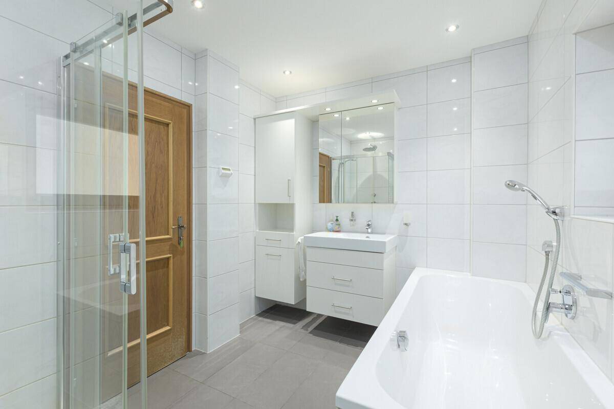Modernes Badezimmer mit weißen Fliesen, Dusche, Badewanne und einem einzelnen Waschbecken.