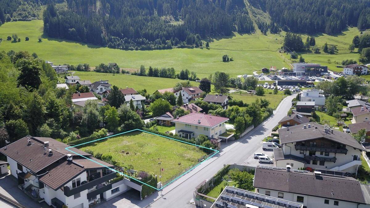 Luftaufnahme eines Baugrundstücks mit grüner Umrandung, umgeben von Wohnhäusern und ländlicher Landschaft.