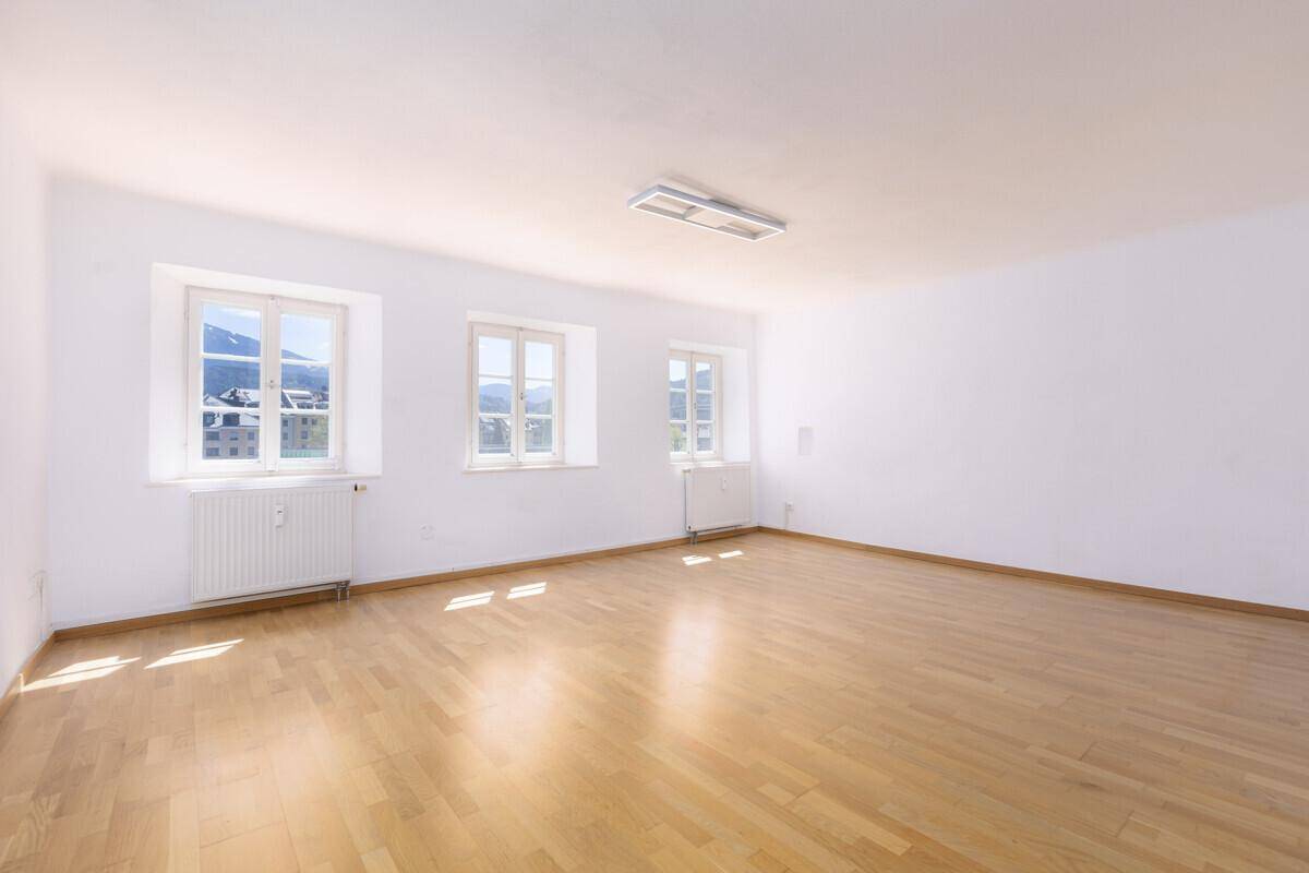 Heller, leerer Raum mit Parkettboden, weißen Wänden und Blick auf die Berge.