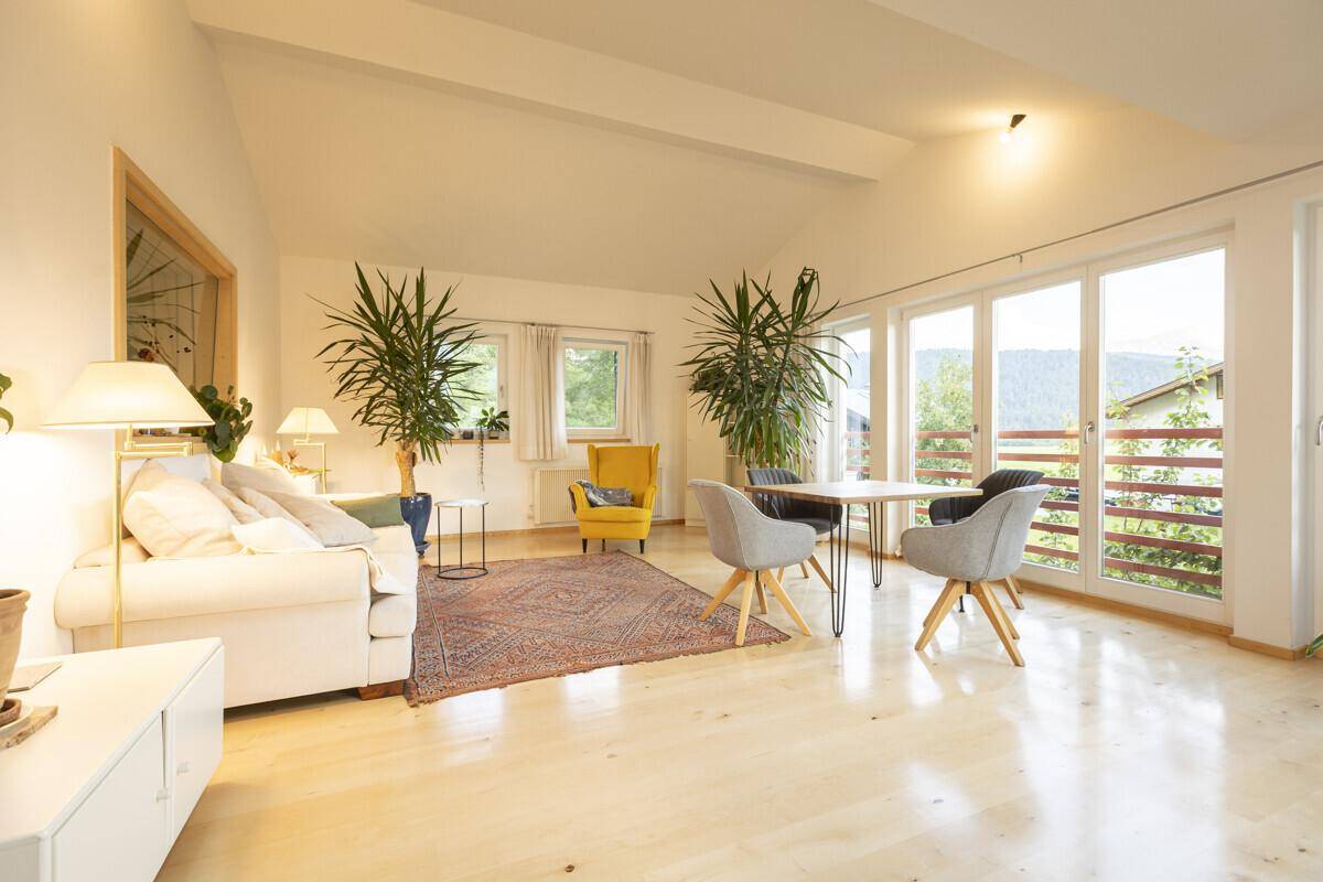 Lichtdurchflutetes Wohnzimmer mit Holzboden, großen Fenstern und Zugang zum Balkon.