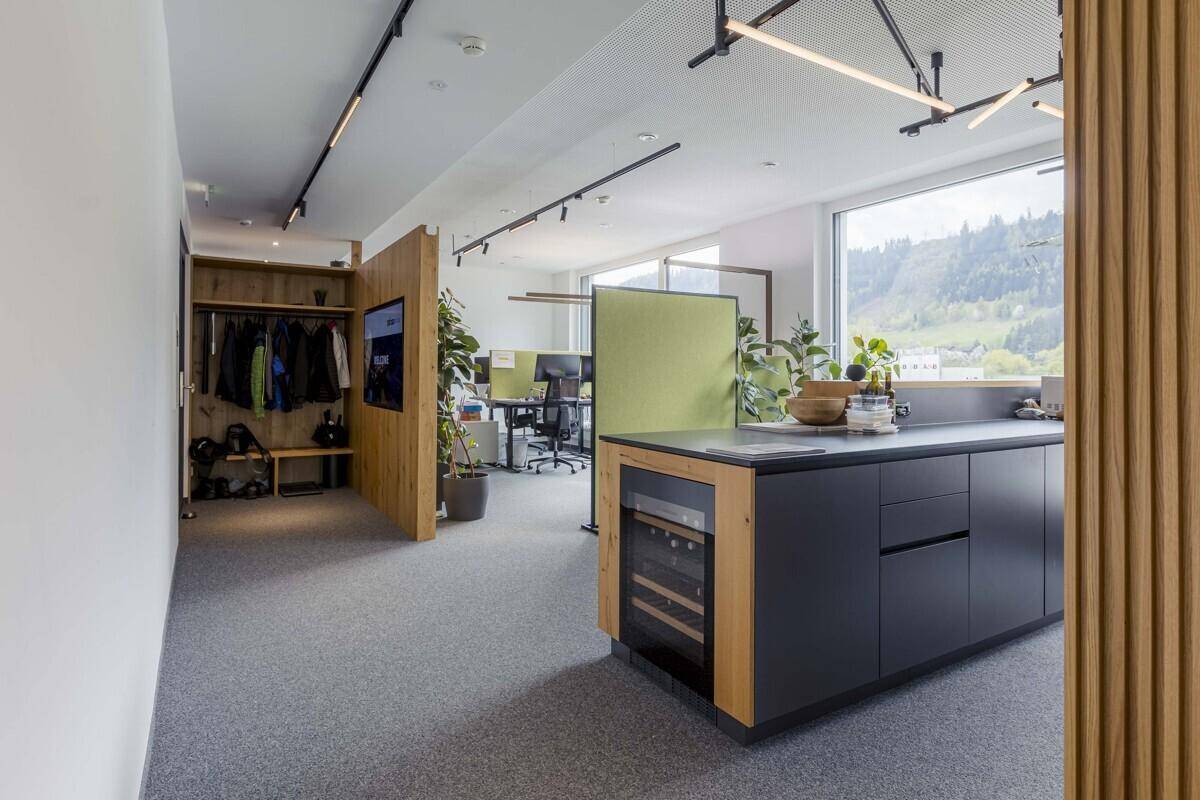 Offener Bürobereich mit integrierter Küchenzeile, Garderobe und modernen Arbeitsplätzen.