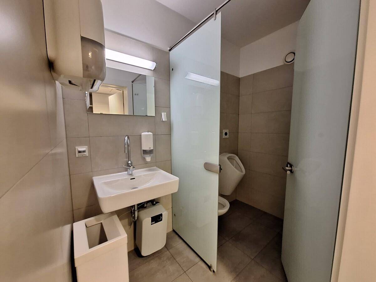 Gewerbliche Toilette mit Urinal, Waschbecken und Fliesen an Wänden und Boden in modernem Design.