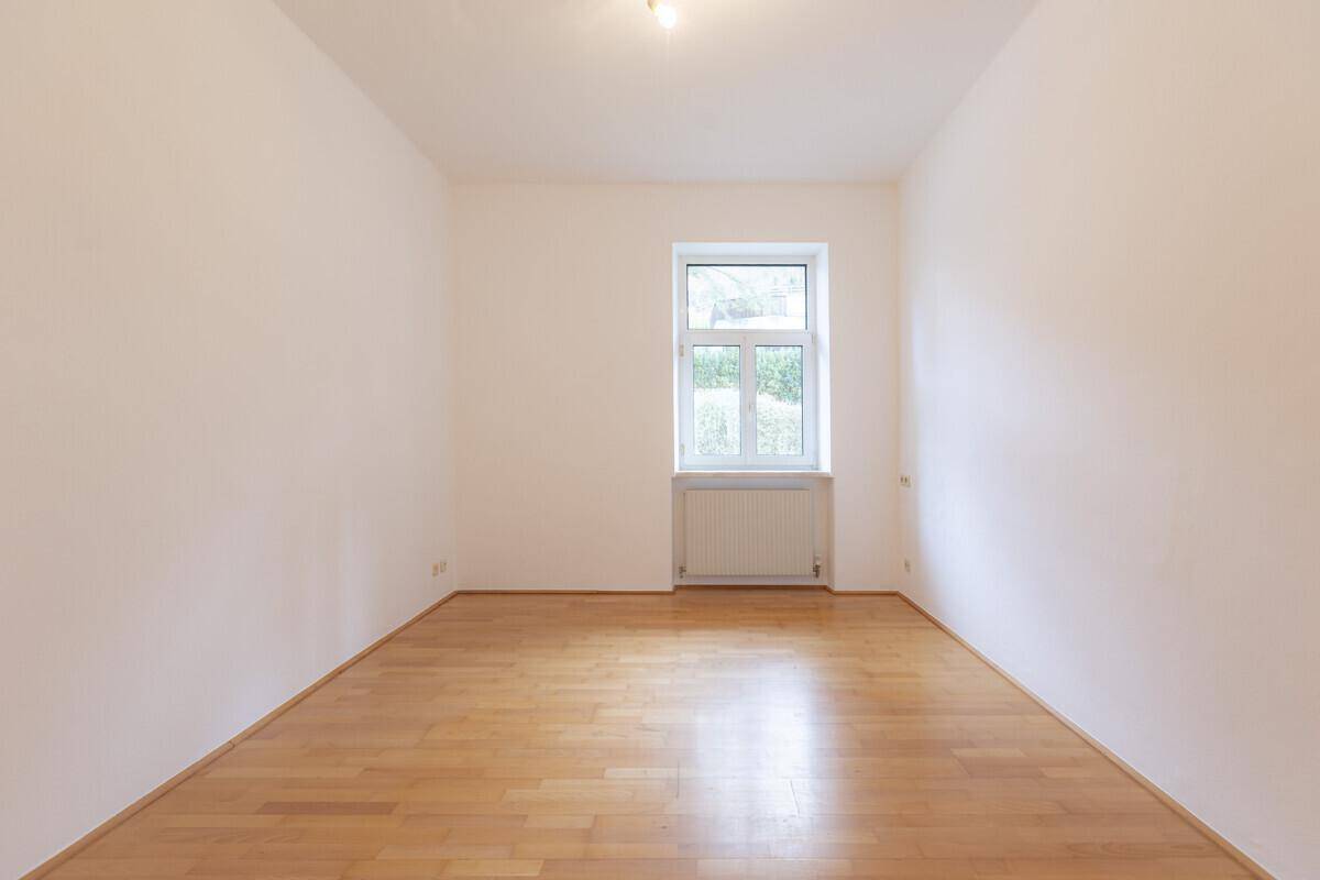 Helles Zimmer mit Holzboden und Blick ins Grüne durch das große Fenster.