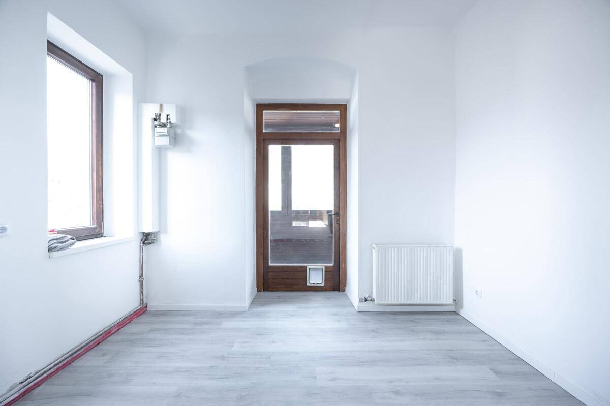 Heller Raum mit Laminatboden, zwei Fenstern und Zugang zu einem Außenbereich.