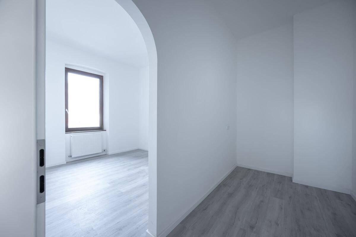 Heller Raum mit Laminatboden und einem Fenster, verbunden durch einen Rundbogen.