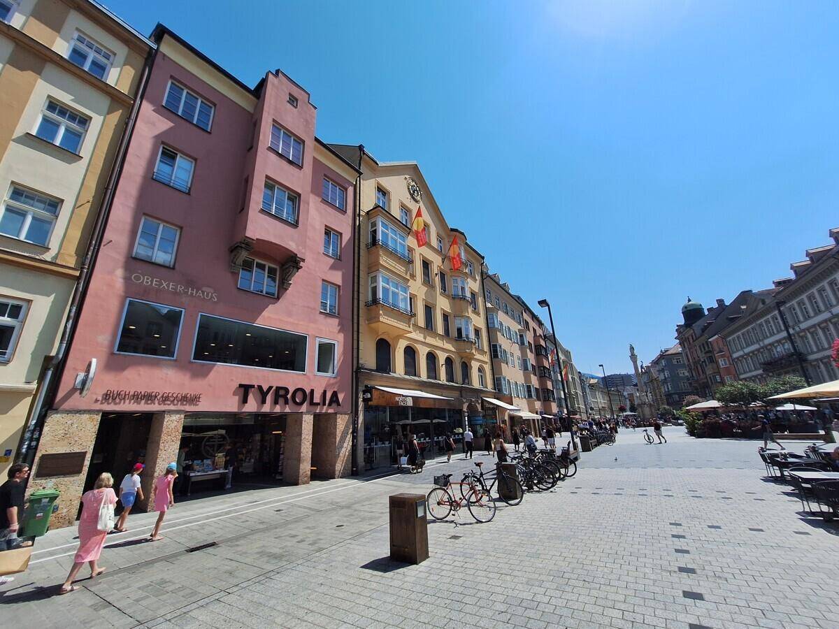 Belebte Einkaufsstraße mit historischen Gebäuden und Geschäften unter blauem Himmel.