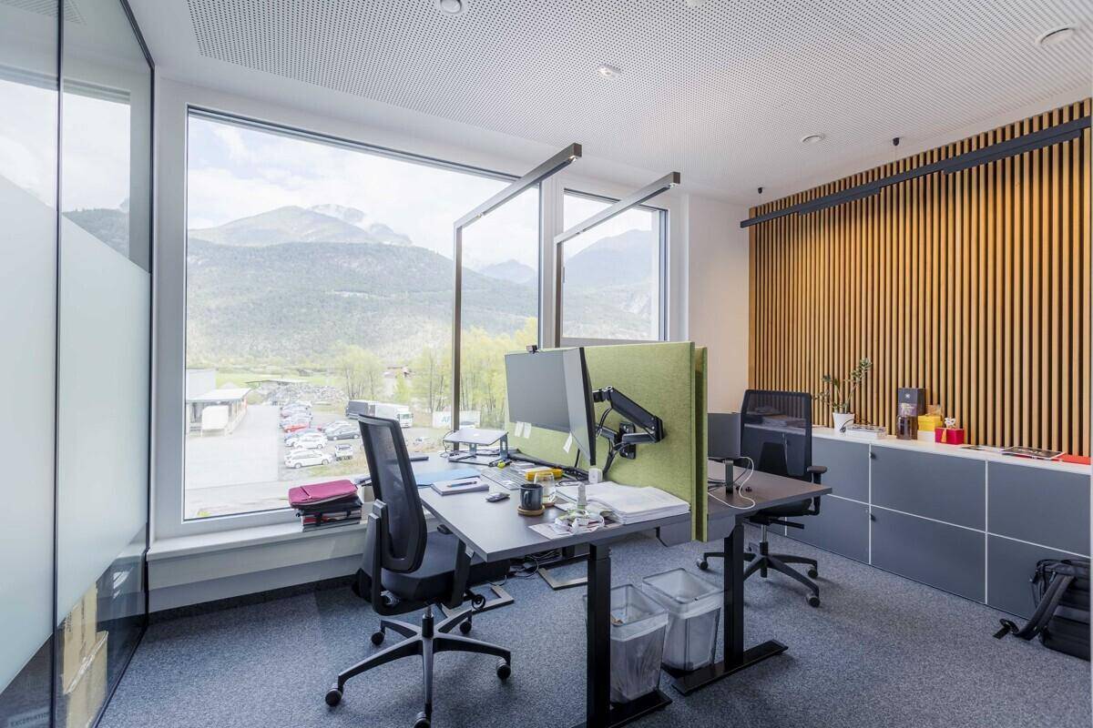 Moderner Büroarbeitsplatz mit Holzlamellenwand, Stauraum und Panoramablick auf die Berge.