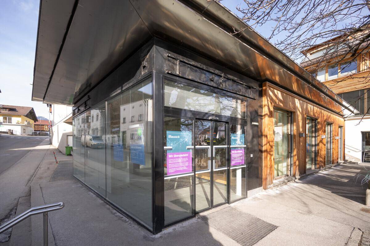 Eingangsbereich des modernen Gebäudes mit Glasfront und Holzverkleidung, von der Straßenseite aus gesehen.