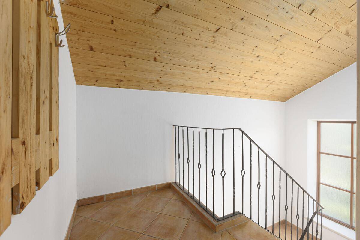 Treppenhaus mit Holzdecke, Fliesenboden und schmiedeeisernem Geländer.