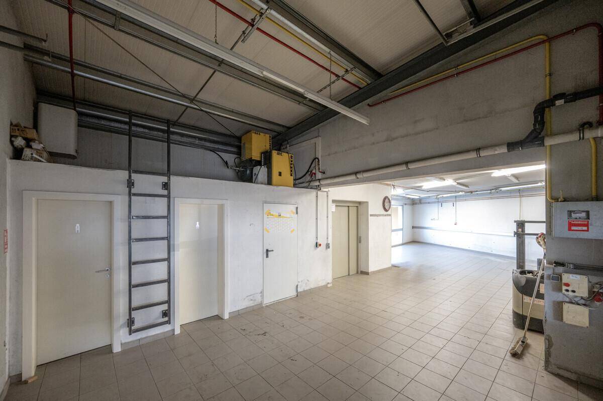 Industrieller Innenraum mit hohen Decken, sichtbaren Installationen, einer Leiter zu einer erhöhten Plattform und einem Aufzug.