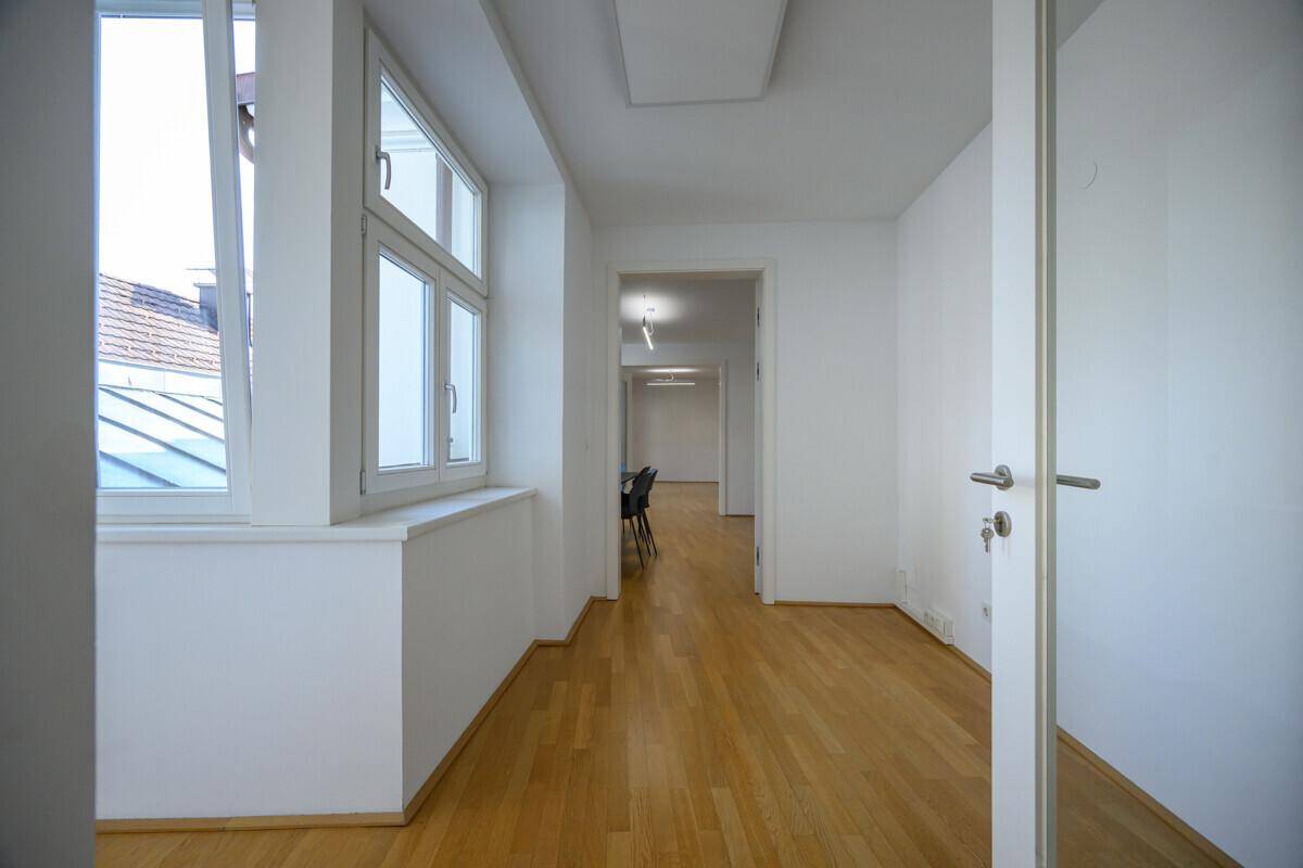 Heller Flur mit Holzboden und Fenstern, der zu weiteren Räumen führt.