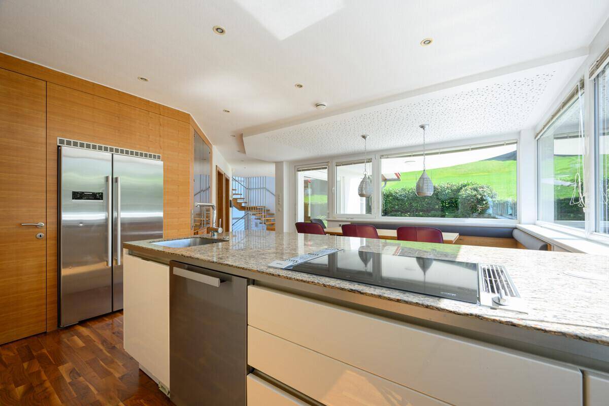 Kücheninsel mit Induktionskochfeld und Spüle, umgeben von Holzvertäfelung und großen Fenstern.
