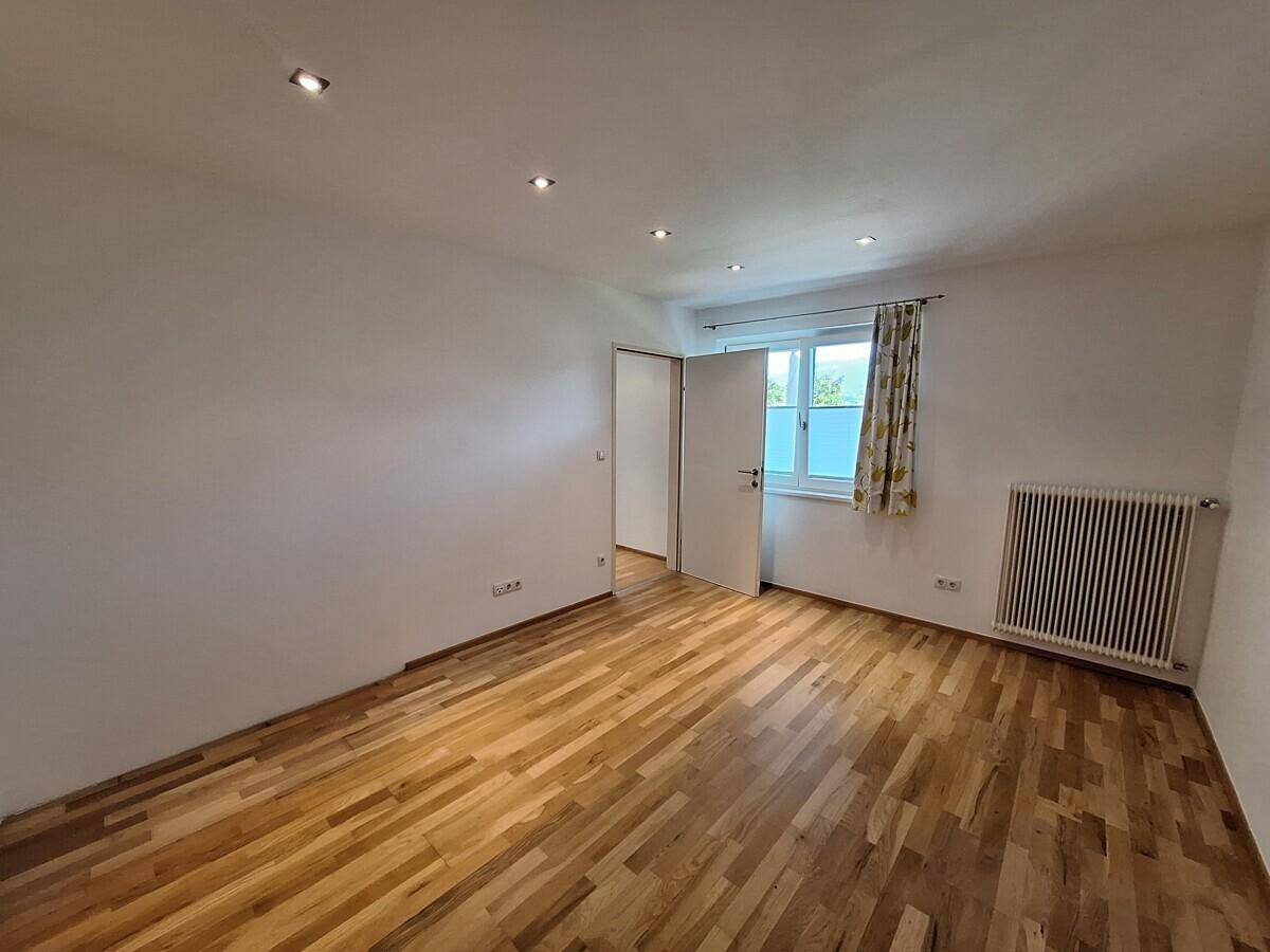 Leerer Raum mit Parkettboden, Fenster und Heizkörper, bereit zur individuellen Gestaltung.