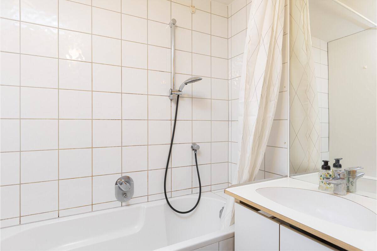 Badezimmer mit weißen Fliesen, Badewanne und Duschvorhang, funktional und hell.