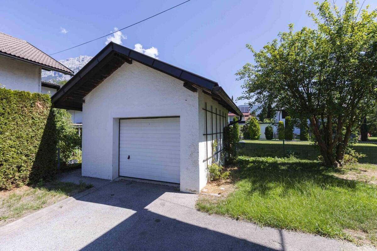Einzelgarage mit weißer Fassade und Schwingtor, umgeben von Grünflächen.