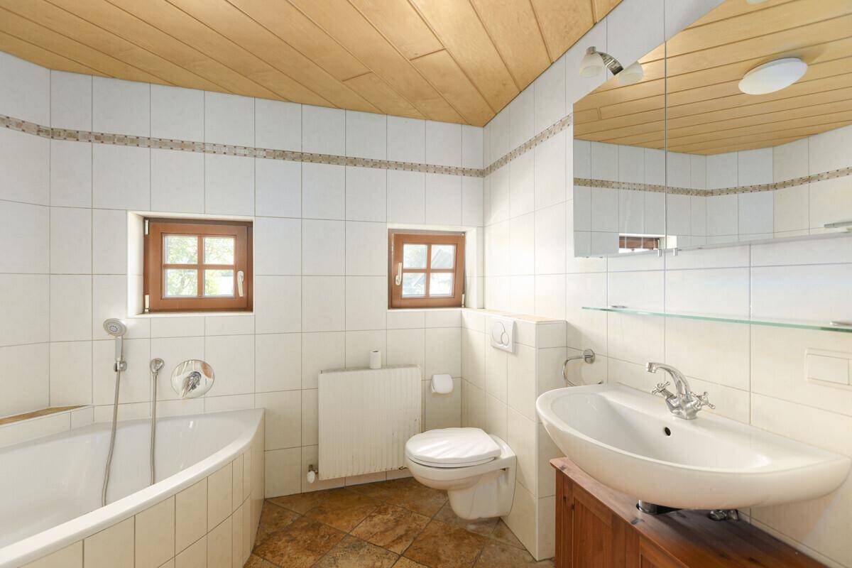 Helles Badezimmer mit weißen Fliesen, Holzdecke, Badewanne und Fenster.