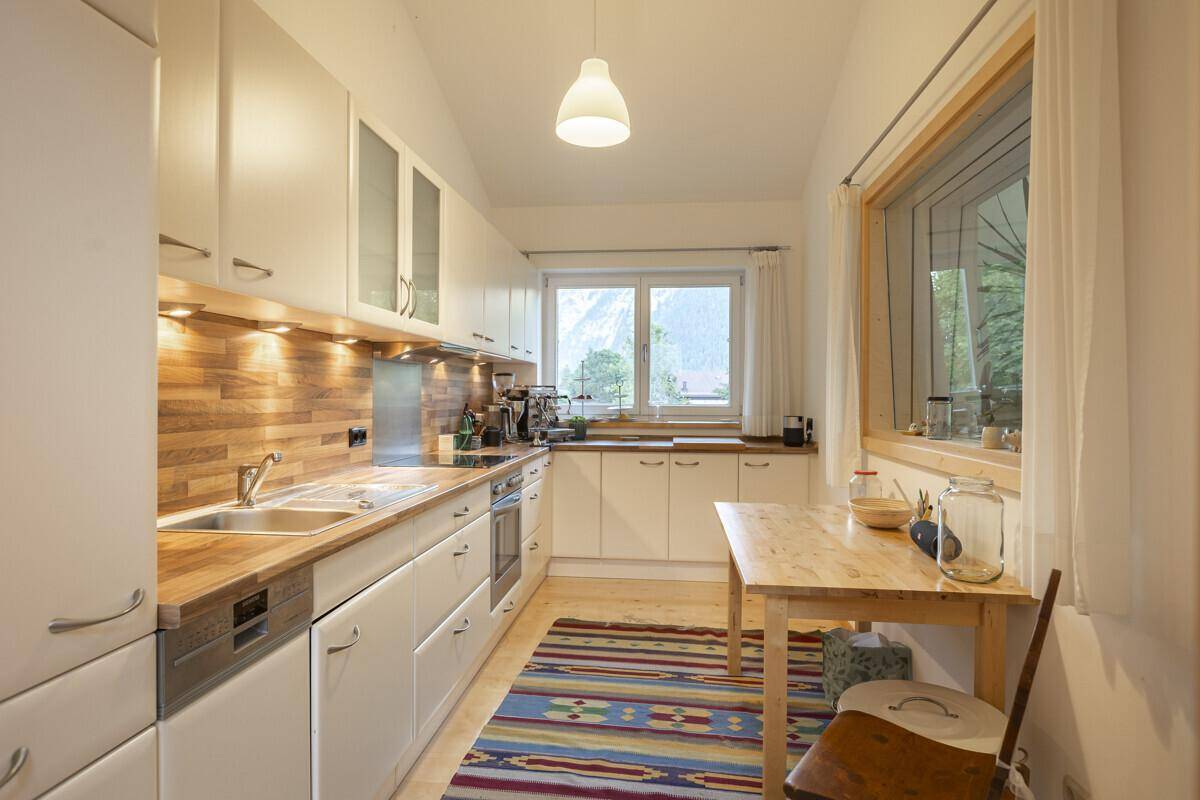 Helle Küche mit weißen Schränken, Holzarbeitsplatte und Fenster mit Bergblick.