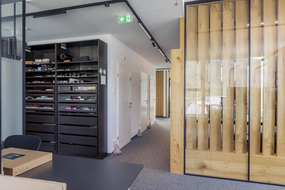 Heller Büroflur mit integrierten Regalen, weißen Türen und einer Holzwand mit Glaselementen.