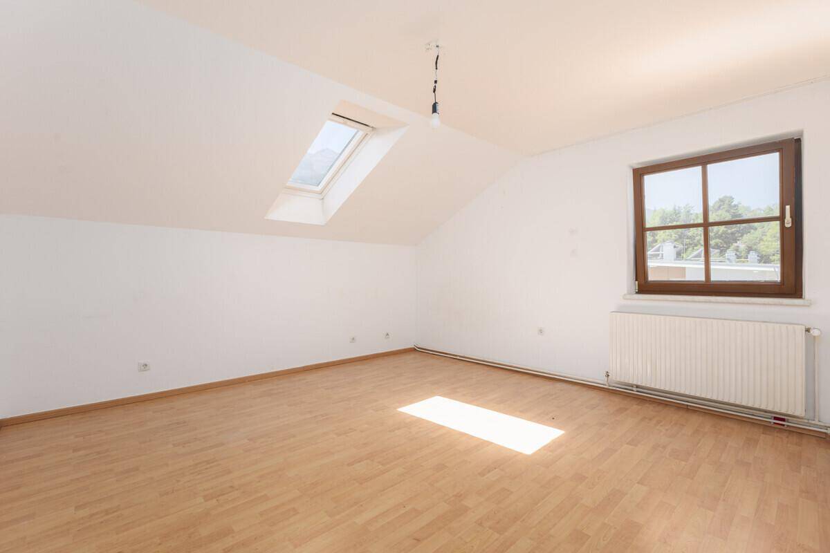 Helles Zimmer im Dachgeschoss mit Laminatboden, Dachfenster und Heizkörper.