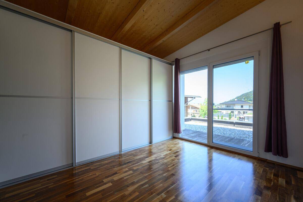 Helles Schlafzimmer mit Einbauschränken, Holzboden und Zugang zu einer Terrasse.