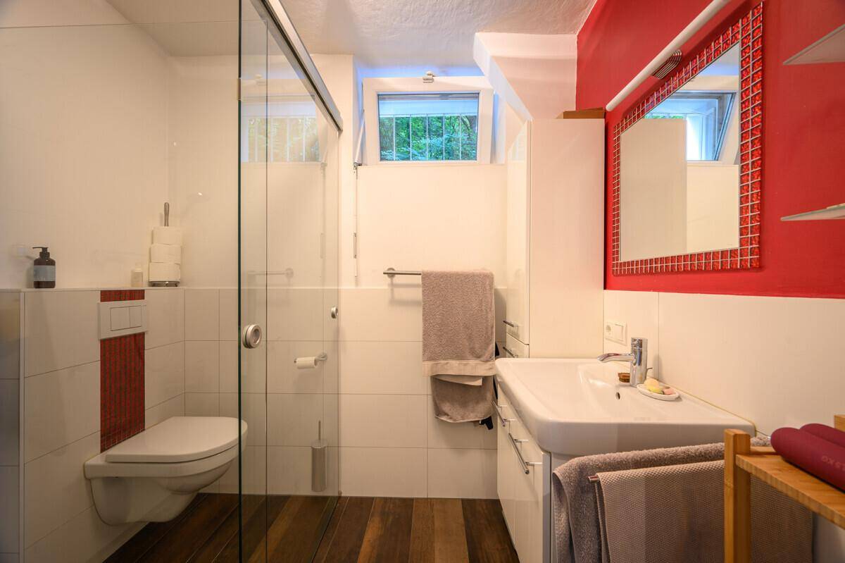 Modernes Badezimmer mit begehbarer Dusche, wandhängendem WC und einem roten Akzent an der Wand.