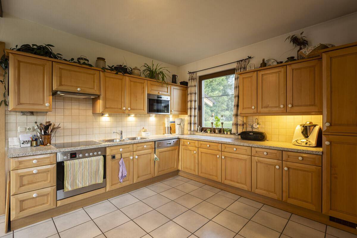 Funktionale Küche mit Holzschränken, Fliesenboden und Fenster mit Blick ins Grüne.