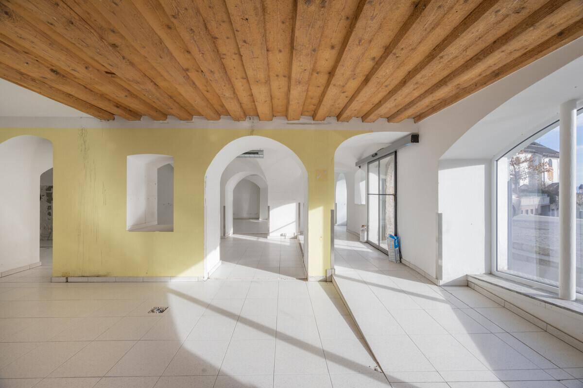 Heller Gewerberaum mit Holzbalkendecke, Fliesenboden, gelben Wänden und großen Fenstern.