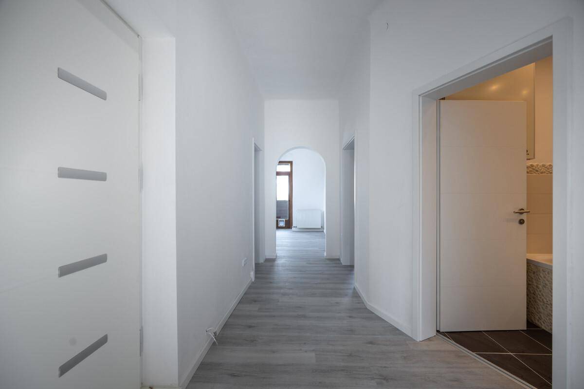 Langer, heller Flur mit modernem Laminatboden und weißen Türen.