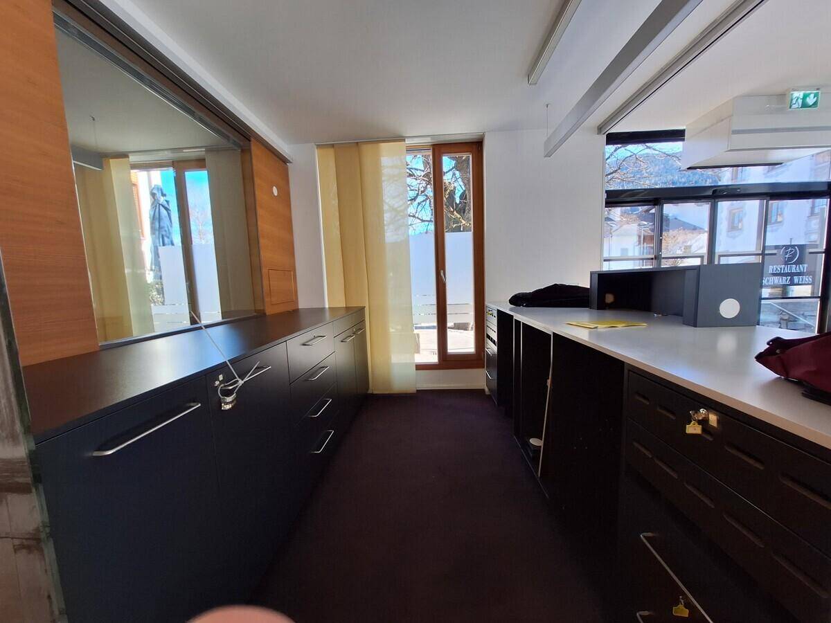Büro mit dunklen Einbauschränken, Teppichboden und einem Fenster mit vertikalen Jalousien für Privatsphäre.