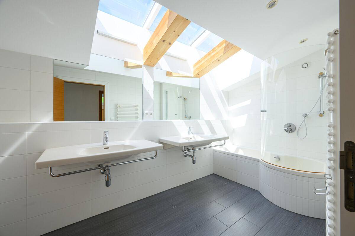 Modernes Badezimmer mit Doppelwaschbecken, Badewanne, Dusche und großem Oberlicht.