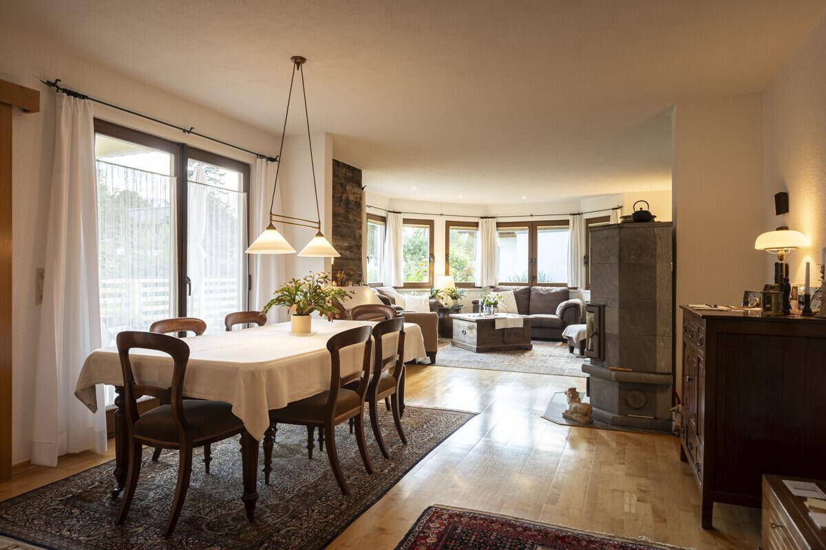 Offener Wohn- und Essbereich mit Holzboden, Kachelofen und Zugang zur Terrasse.