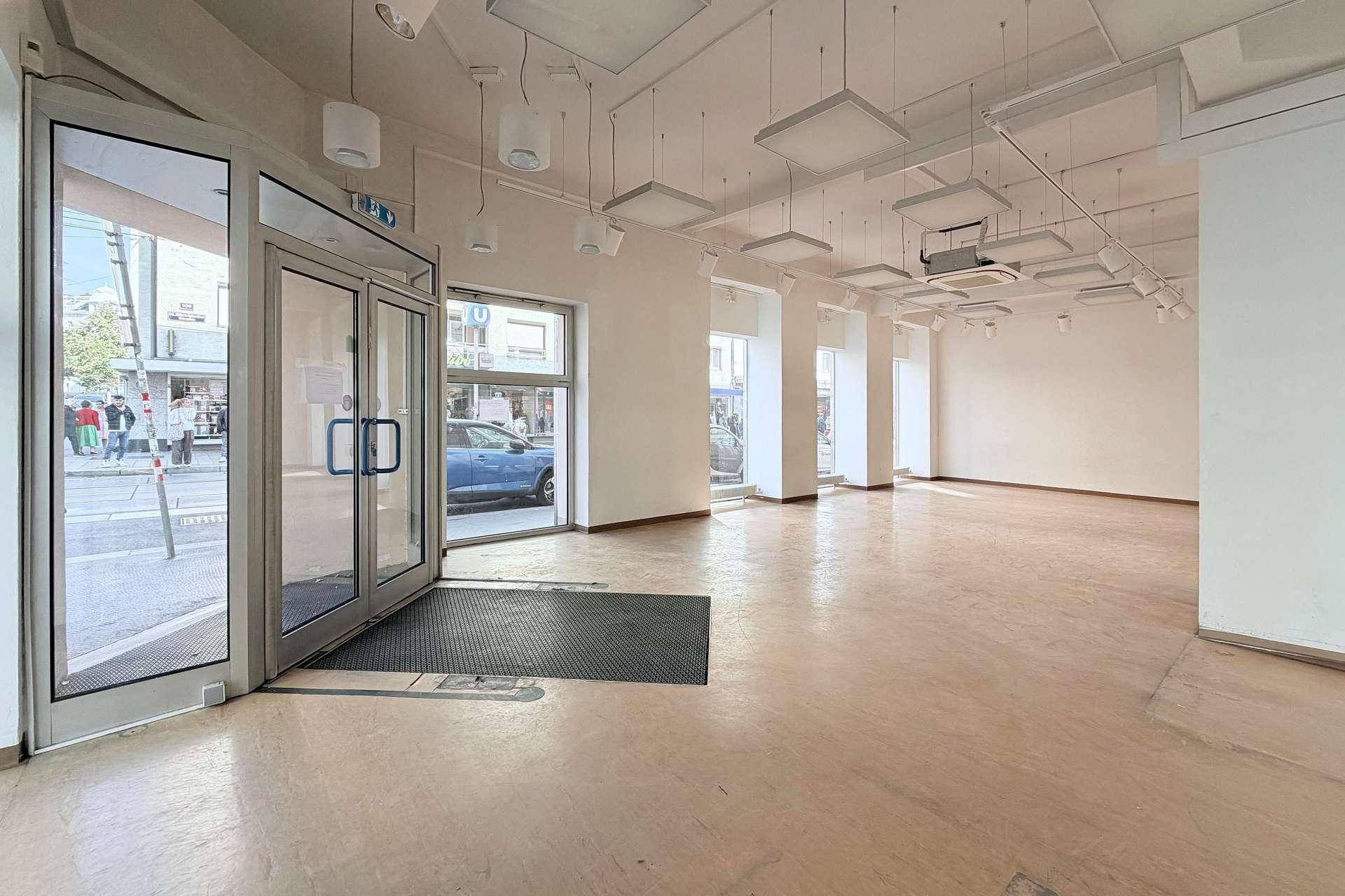Eingangsbereich eines Geschäftsraums mit großen Glastüren und Schaufenstern zur belebten Straße.