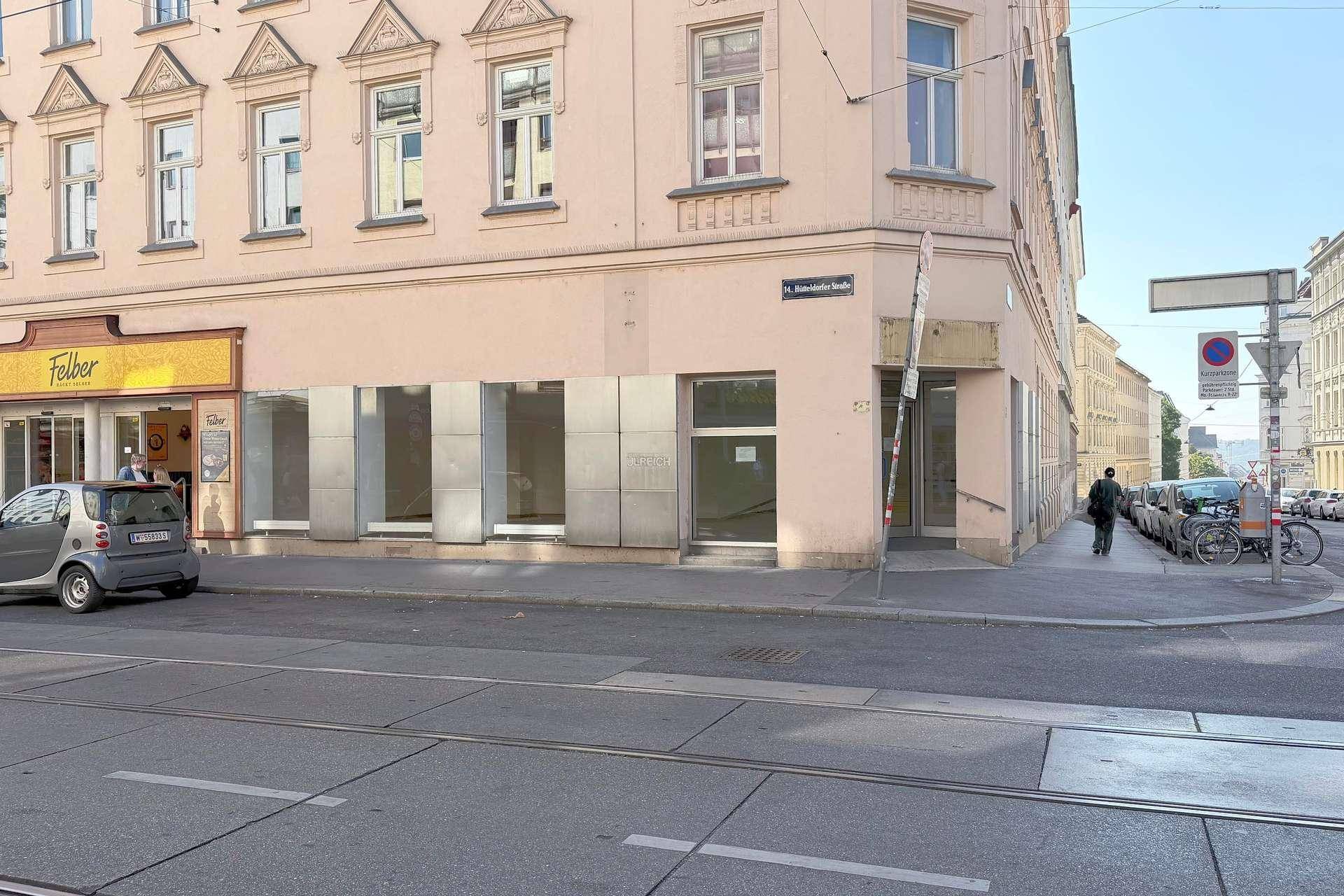 Eckgebäude mit Schaufenstern im Erdgeschoss und Straßenbahnschienen im Vordergrund.