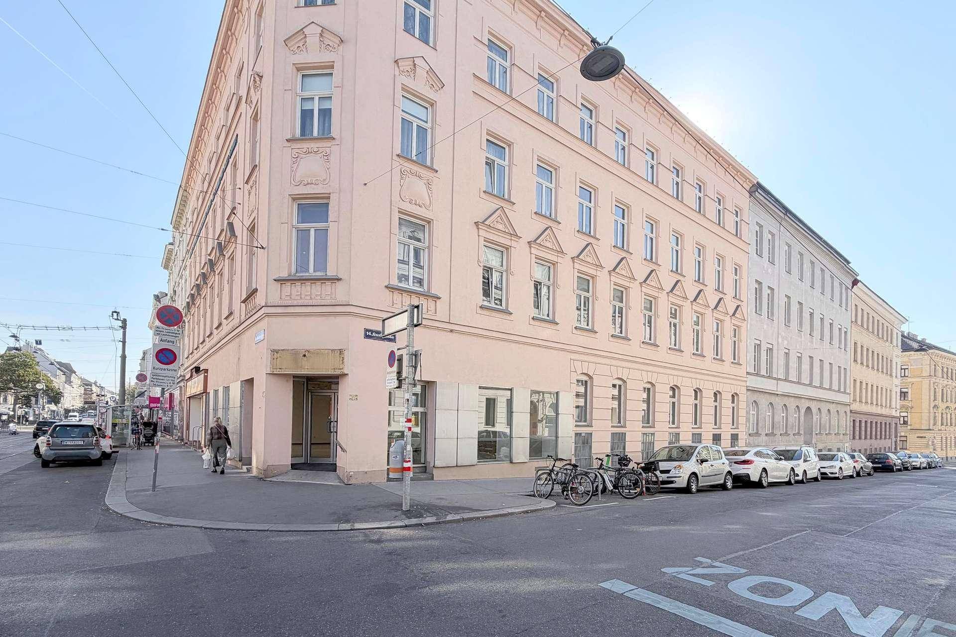 Historisches Eckgebäude mit rosafarbener Fassade und vielen Fenstern an einer belebten Straße.
