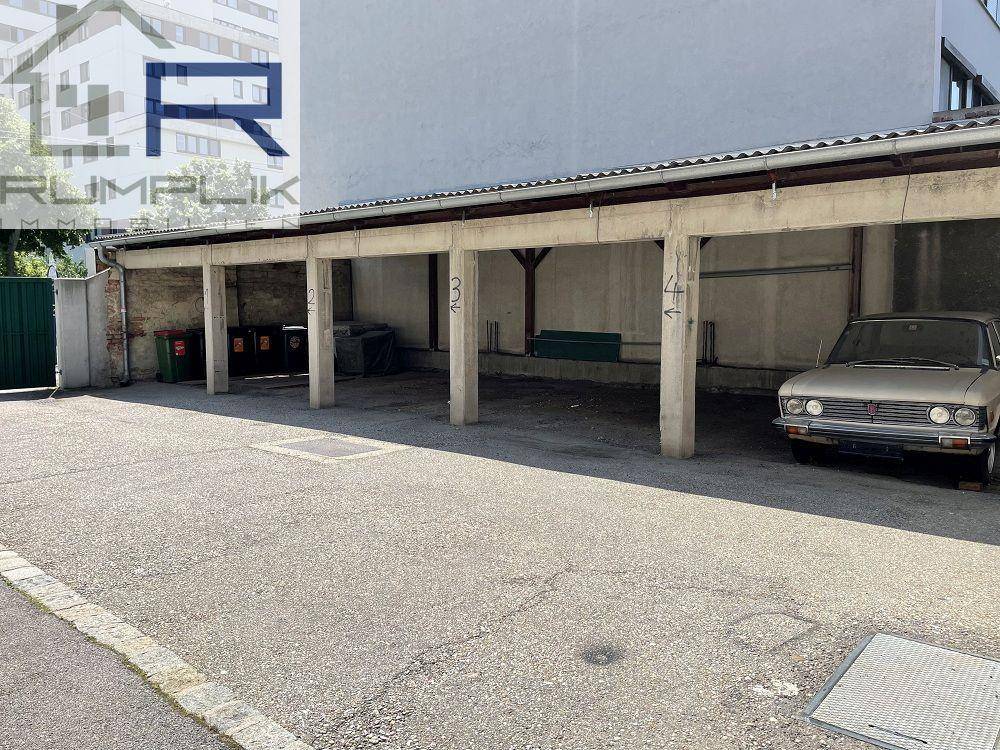 Außenparkplatz mit überdachten Stellplätzen aus Beton und einem älteren Fahrzeug.