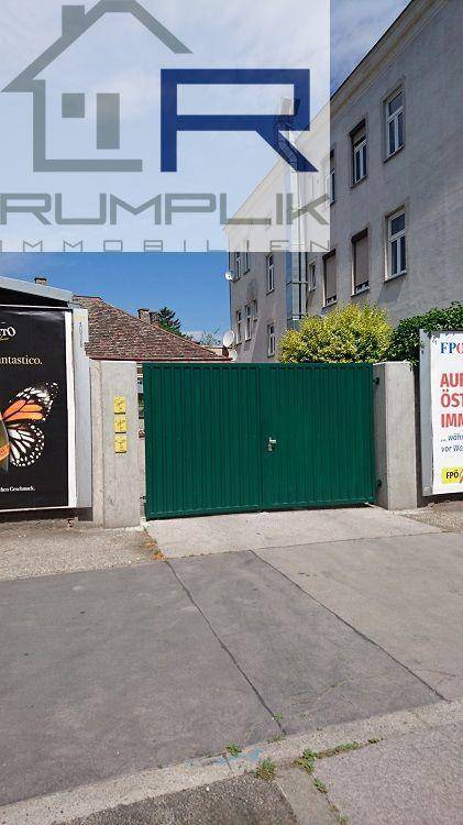 Grünes Metalltor als Zufahrt zu einem Grundstück mit umliegenden Gebäuden.