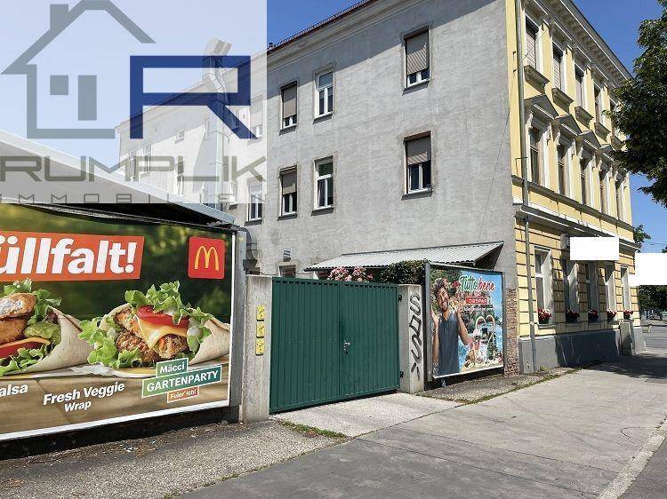Seitenansicht des Gebäudes mit grauer Fassade, einem grünen Tor und großen Werbetafeln.