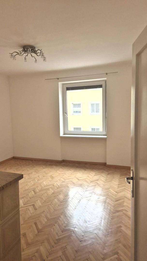 Helles Wohnzimmer mit Fischgrätparkett und einem Fenster mit Blick auf ein gegenüberliegendes Gebäude.