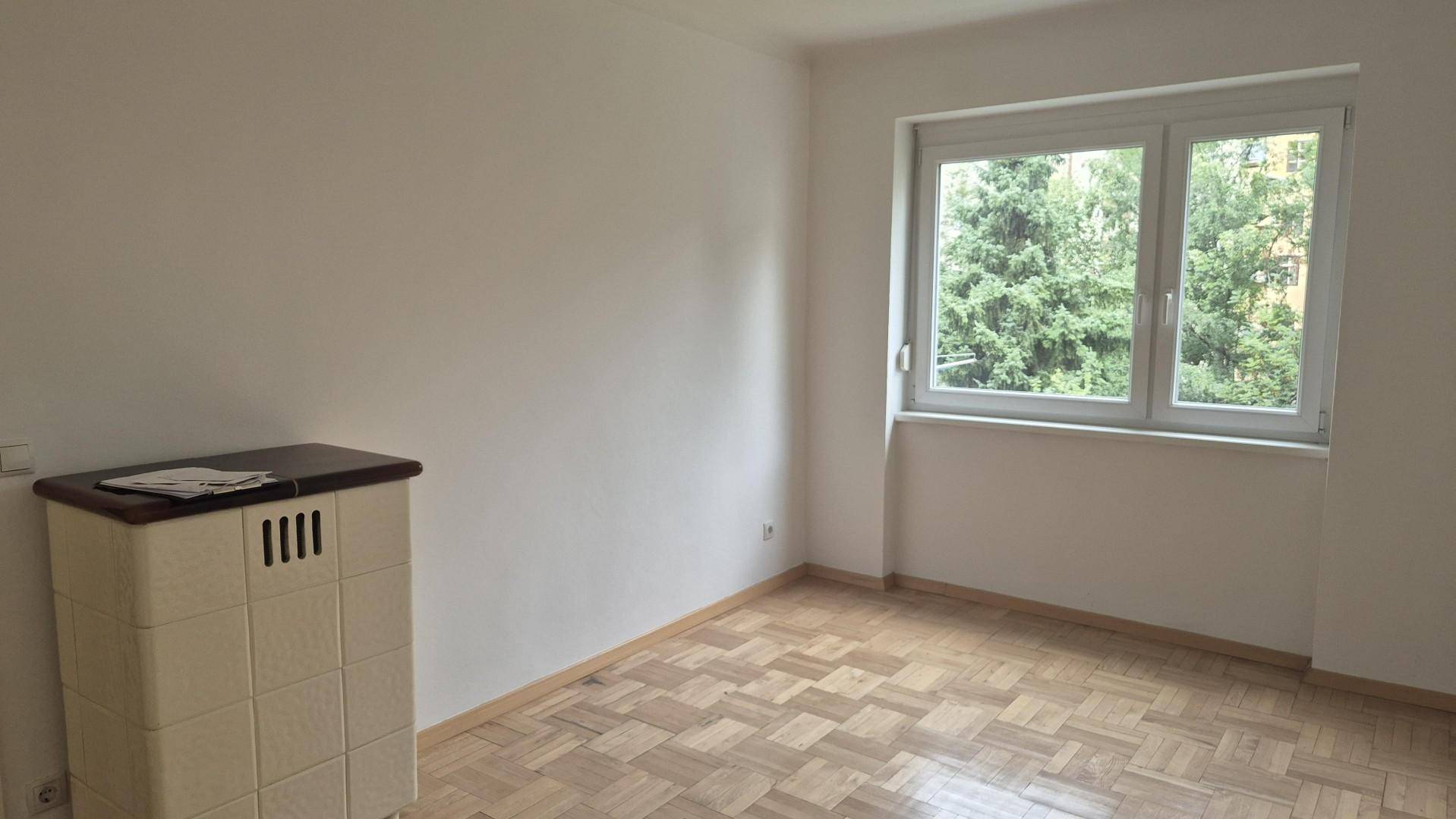 Ruhiges Schlafzimmer mit Parkettboden und Fenster mit Blick auf Bäume.