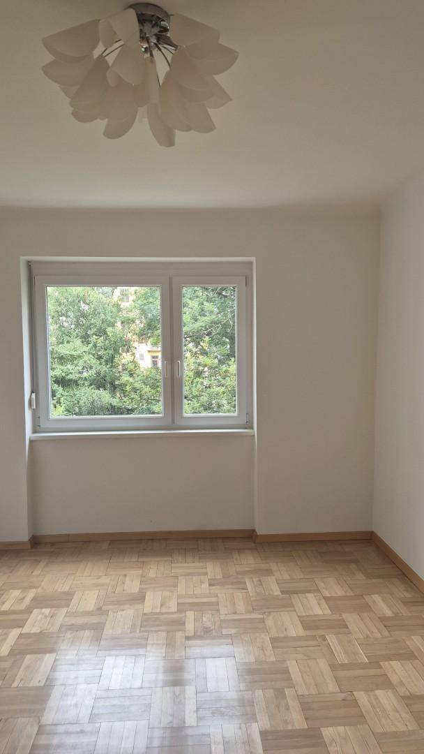 Schlafzimmer mit hellem Parkettboden und Fenster mit Blick ins Grüne.