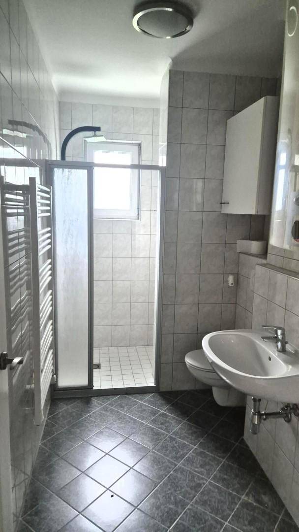 Modernes Badezimmer mit grauen Fliesen, Duschkabine, WC und beheiztem Handtuchhalter.