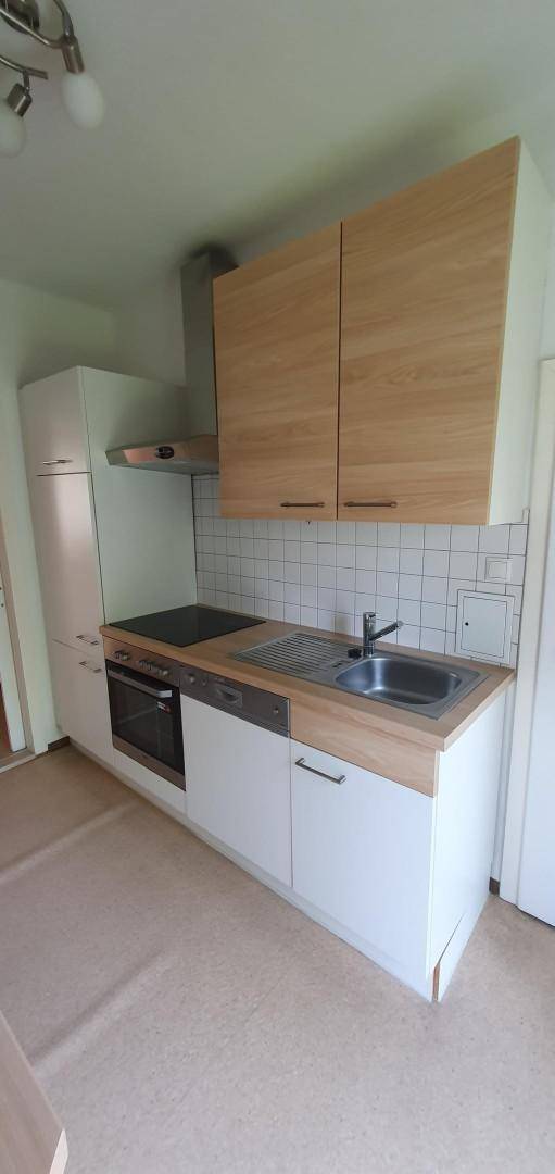 Funktionale Küche mit hellen Holzschränken, weißen Fliesen und integrierten Geräten.
