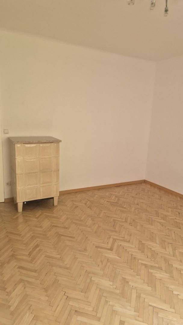 Geräumiges Wohnzimmer mit klassischem Fischgrätparkett und heller Wandgestaltung.