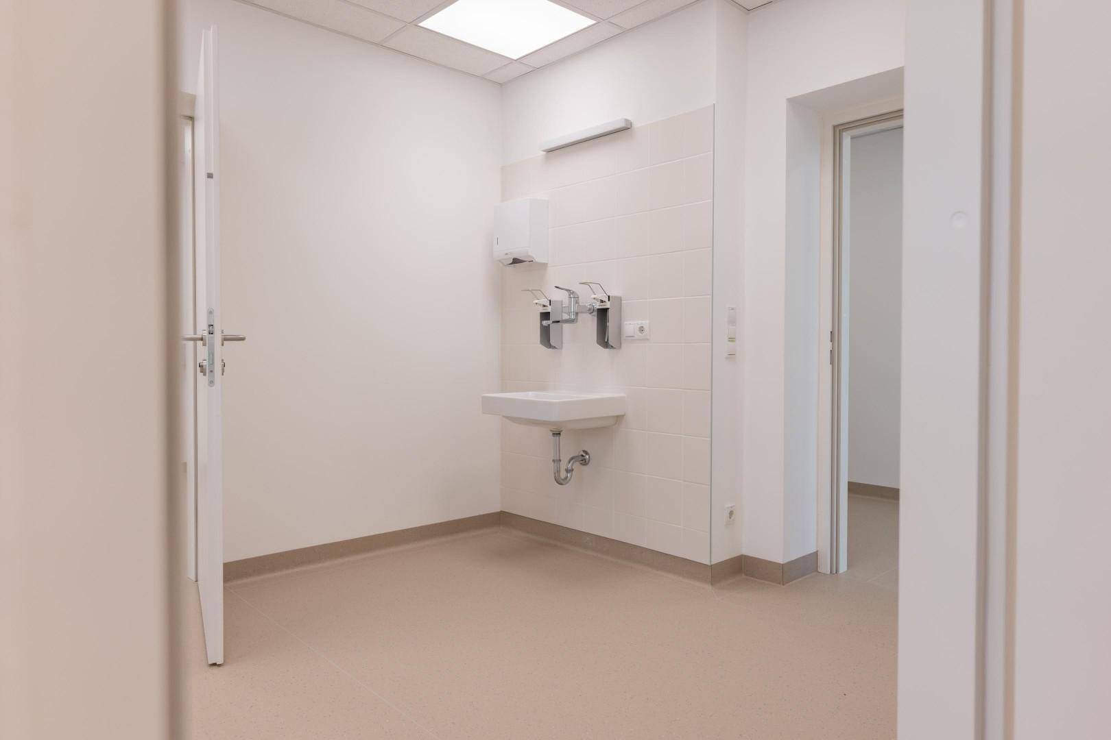 Funktionaler Waschraum mit wandmontiertem Waschbecken und Spendern, ideal für den gewerblichen Gebrauch.