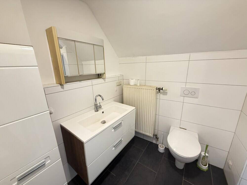 Modernes Badezimmer mit Waschtisch, Spiegelschrank, Wand-WC und dunklem Fliesenboden unter Dachschräge.