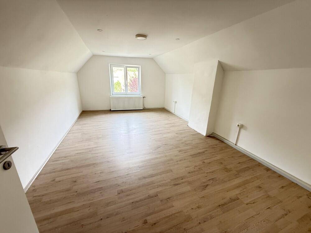 Geräumiges Zimmer im Dachgeschoss mit Laminatboden, weiß gestrichenen Wänden und Dachschrägen.