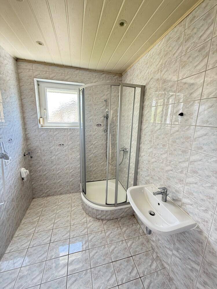 Gefliestes Badezimmer mit Eckdusche, Einzelwaschbecken und einem Fenster für Tageslicht.