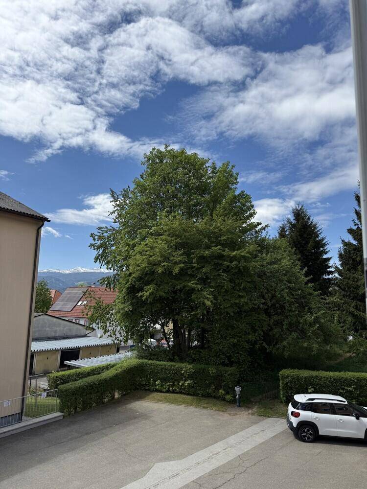 Weiter Ausblick auf einen Parkplatz, grüne Bäume und die umliegende Berglandschaft.